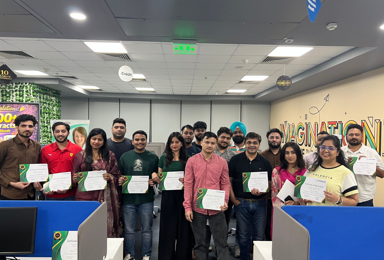 Group of employees posing with certificates in an office celebration event.