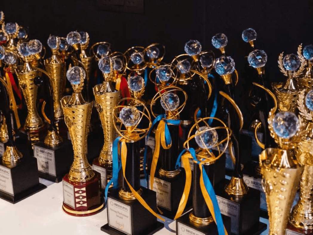 Row of gold trophies with blue and yellow ribbons on a table, prepared for an awards ceremony.