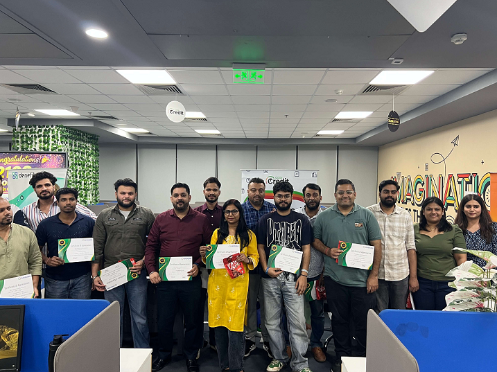 Office group photo: coworkers standing in a modern office, each holding a certificate during a ceremony.