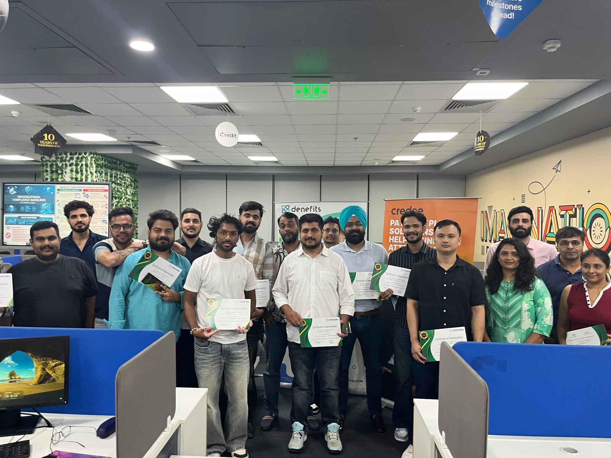 Group of people in an office holding certificates, posing for a photo at a corporate event.
